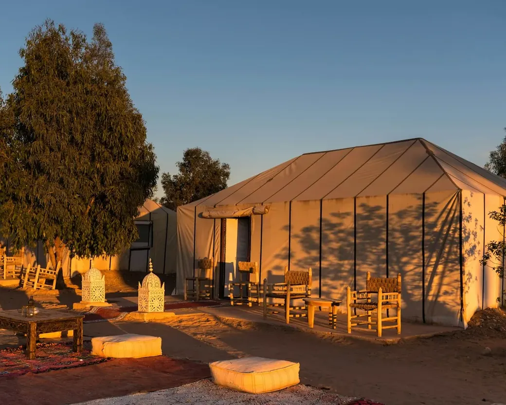 Canvas tent with lanterns and seating at a desert camp in warm evening light near Merzouga